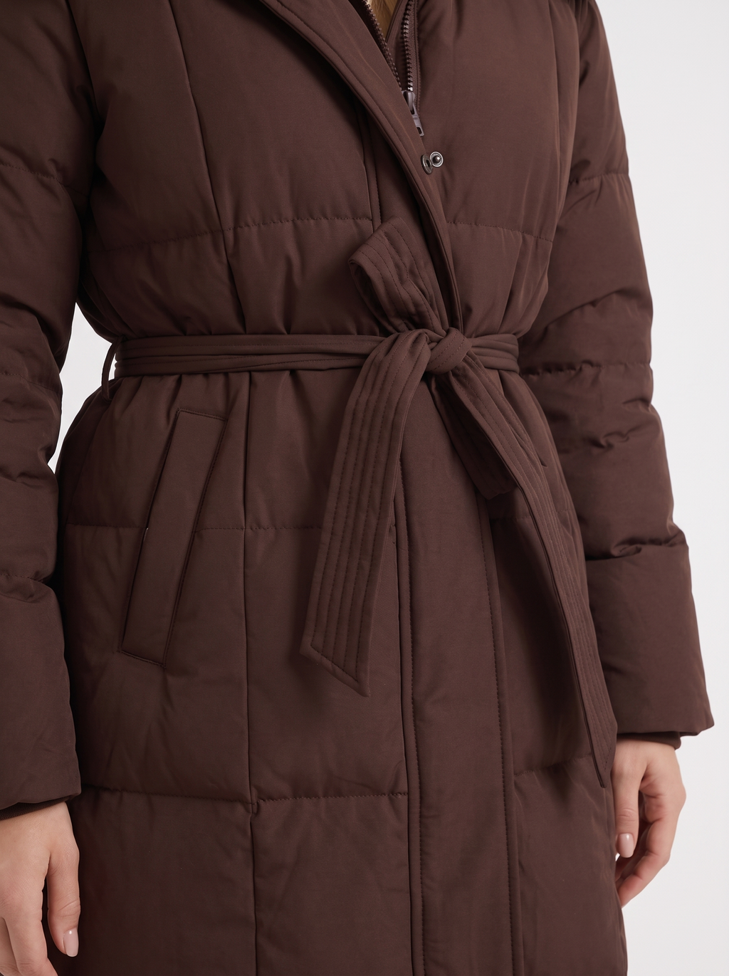 Woman wearing a long hooded quilted puffer jacket with tie belt - view 12