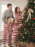 Family wearing matching red and white candy cane striped Christmas pajamas by the tree