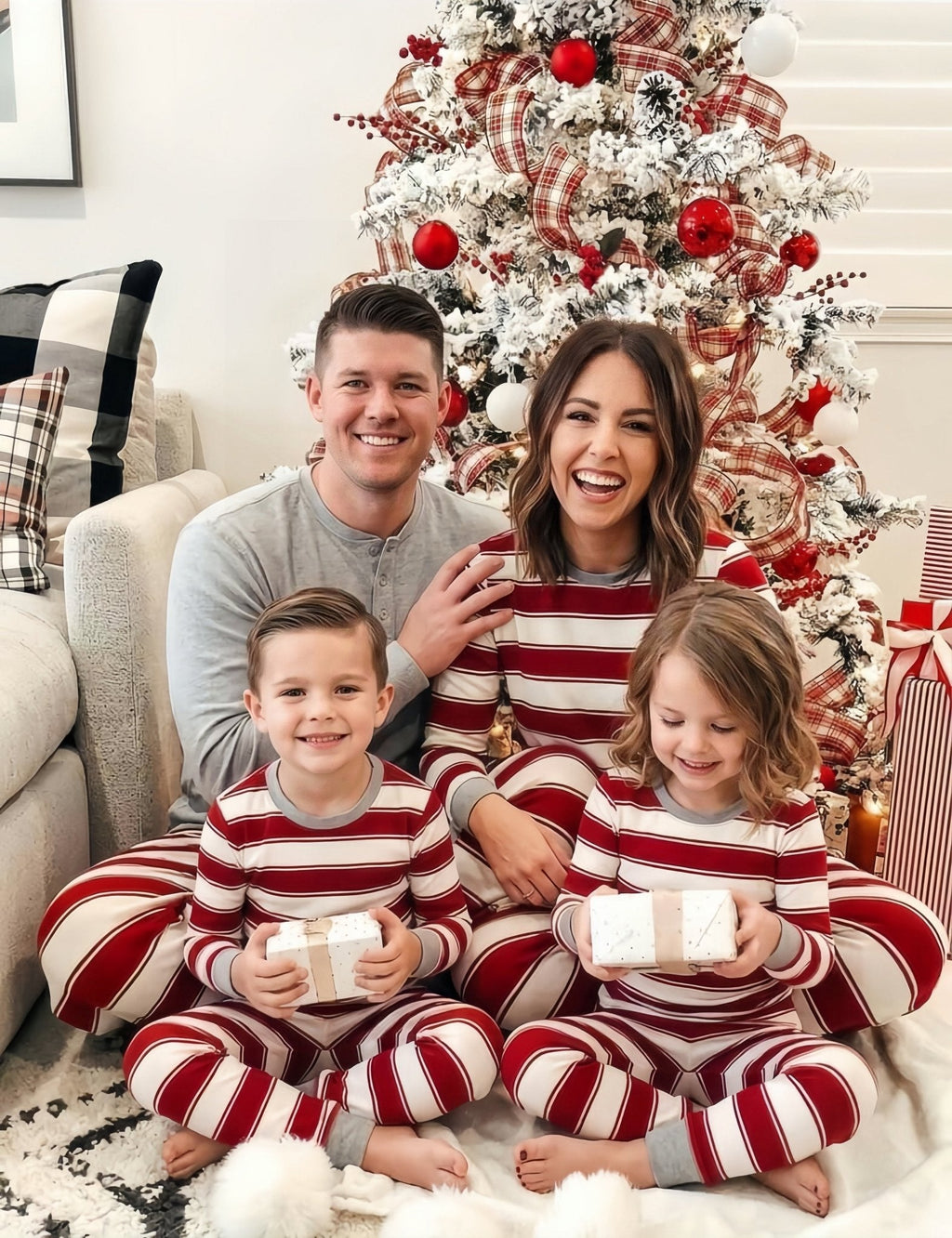 Family wearing matching red and white candy cane striped Christmas pajamas by the tree - view 4