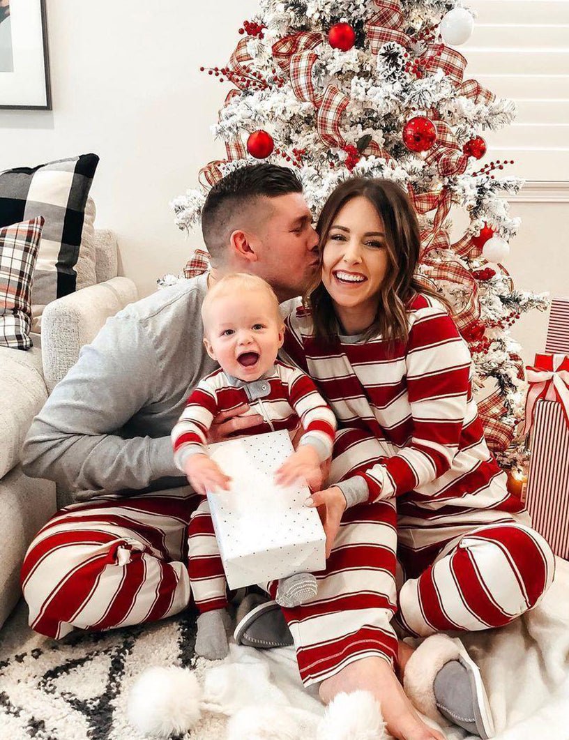 Family wearing matching red and white candy cane striped Christmas pajamas by the tree - view 7