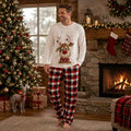 Woman in holiday pajamas with reindeer print top and red black plaid pants beside a Christmas tree - view 2